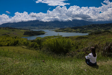 Female tourist sitting looking at the biggest artificial lake in Colombia called Calima Lake located on the mountains of Darien at the region of Valle del Cauca