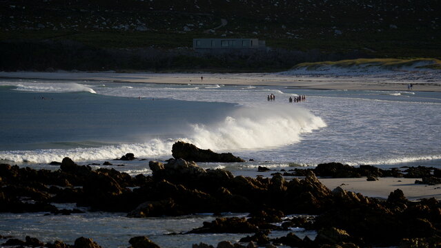 Powerful ocean waves breaking near a sandy beach with a group of people standing on the shore in Cape Town South Africa
