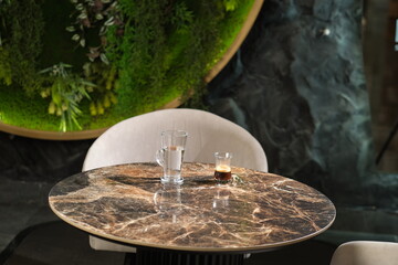 Marble table with a glass of water and espresso in a stylish interior featuring a green wall and...