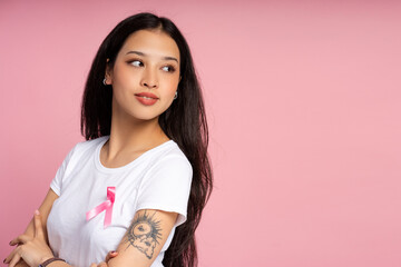Young woman wearing pink ribbon is looking over shoulder on pink background
