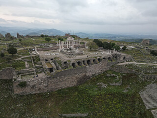 Aerial view of Pergamon Acropolis on a mountain in Bergama Turkey The site features ancient columns walls and courtyards Tourists walk among the ruins surrounded by lush hills and cloudy horizons