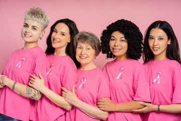 Group of diverse multinational women embracing and showing pink ribbons for breast cancer awareness