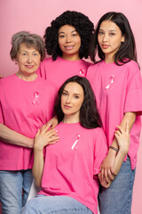 Portrait of group of diverse women embracing and showing pink ribbons for breast cancer awareness