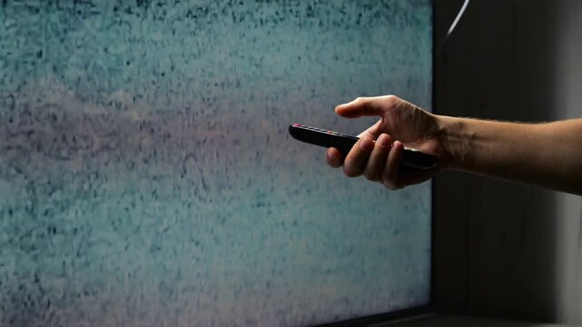 Male hand anf broken TV with white noise on screen.
Close-up of TV static and white noise on screen.
Broken TV and hand with remote control