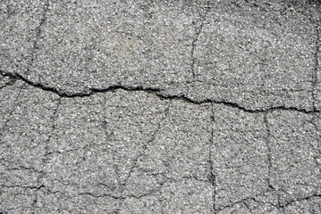 Detailed macro view of rough asphalt pavement with scattered gravel and natural crack patterns, ideal for texture backgrounds and graphic design projects.