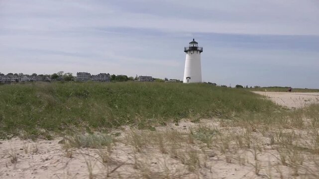 A lighthouse stands tall on a grassy dune overlooking the ocean on cape cod