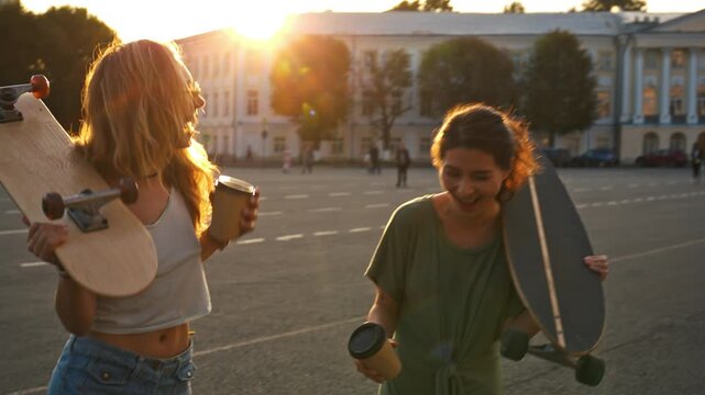Close-up portrait of two laughing girl friends drinking coffee on a city street. Pretty smiling teenagers are hanging out enjoy time together with a skateboard and happy vibes