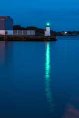 Harbor lighthouse glowing green over the calm sea at twilight, with reflections stretching across the water.