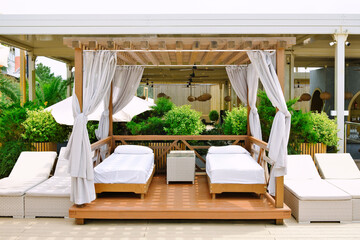Cozy beach cabana with white beds and curtains surrounded by green plants at summer sunny day. Place for the rest on resort.