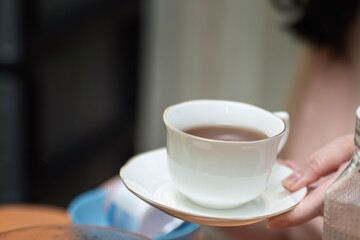A woman's hand receiving an elegant white ceramic cup of black tea on a saucer