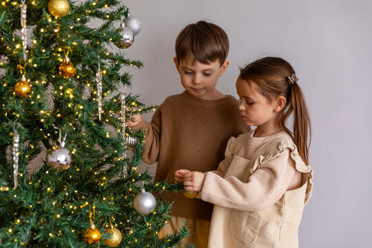 Two children, best friends or siblings are decorating festive Christmas tree in living room at home. Merry Christmas and Happy New year winter holidays. High quality photo