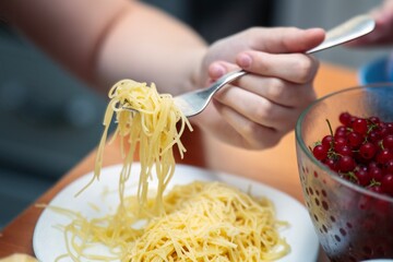 Teenager's hand with a fork full of spaghetti, lifted from a plate of pasta