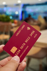A man's hand holding a red credit card against an interior background to make an online payment. Online shopping concept.