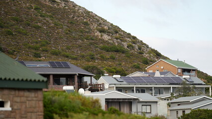 Residential houses with solar panels on rooftops located near green rocky hills in Cape Town
