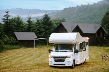 A gleaming white camper sits nestled in a lush green meadow. Rolling hills of the Carpathian...