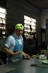 Welder working metal in workshop wearing apron and cap