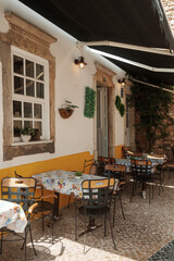 Outdoor café seating with colorful tablecloths under a black awning in Algarve, Portugal.