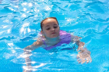 A young girl of mixed ethnicity swims joyfully in a sparkling blue pool, her carefree spirit shining through.