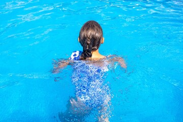 A young girl with brown hair splashes in a vibrant blue swimming pool, enjoying a sunny day of...