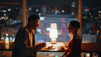 Romantic couple sitting dark restaurant at panoramic window with night city view