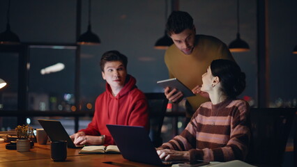 Executive supervising business team working at laptops in dark office closeup.