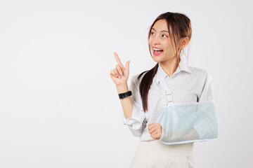Happy asian woman with a broken arm in a cast, arm sling, pointing a finger up with her good hand,...