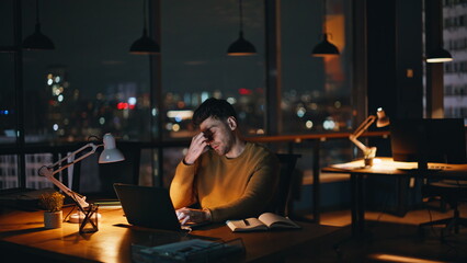 Overworked entrepreneur feeling eyestrain looking laptop at night workplace. 
