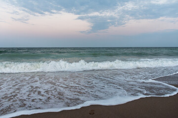 Ocean waves rolling onto foamy sandy shore under pastel evening sky