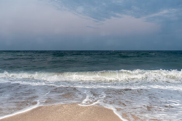 Gentle ocean wave rolling onto sandy beach under cloudy sky