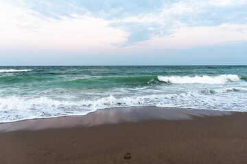 Ocean waves crashing on sandy beach under cloudy sky at sunset