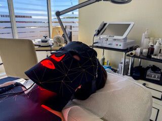Female with a black LED facial mask relaxing in a modern spa setting, showcasing a focus on...