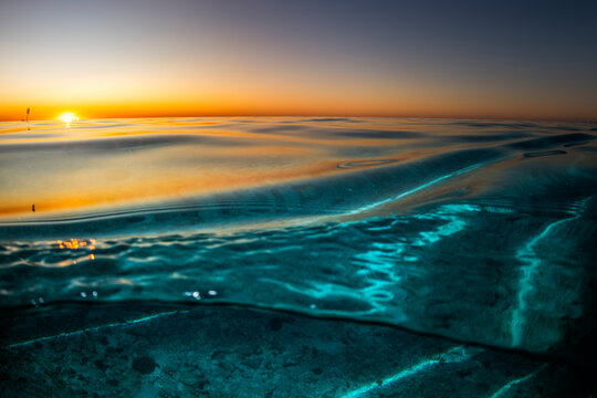 Sunset over Heron Island in Queensland with golden light reflecting on the glassy surface of the ocean. The calm water reveals coral below while a shipwreck silhouette rests on the horizon. - Powered by Adobe