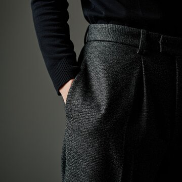 Close-up of a person wearing textured grey trousers with hand in pocket and black long sleeve top, showcasing fashionable casual menswear and stylish outfit details.