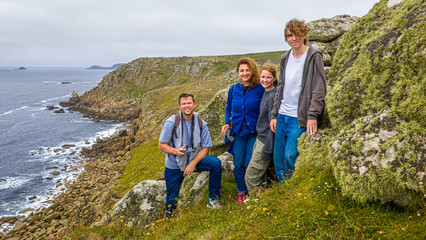 Family of four hiking on a grassy coastal cliff with ocean views