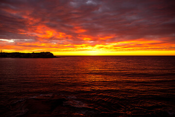 Fiery sunrise over the ocean at Bondi Beach, Sydney, Australia, with glowing clouds reflecting on the water.