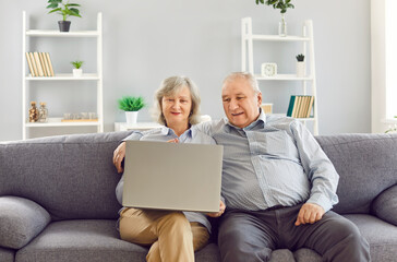 Happy elderly, old couple using a laptop for online entertainment while sitting on the sofa at...