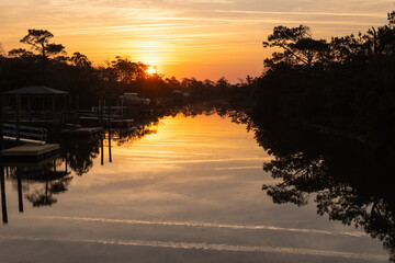 OAK ISLAND, North Carolina, USA - March 13, 2025: A serene sunset reflects across a calm canal lined with docks and trees.