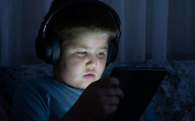 Focused Young Boy Using a Digital Tablet Outdoors. A Child Engrossed in Screen Time While Sitting...