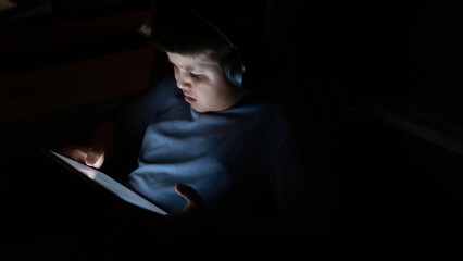 Focused Young Boy Using a Digital Tablet Outdoors. A Child Engrossed in Screen Time While Sitting...