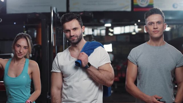 two men and one woman standing in the gym looking at the camera smile feel happy light fitness body strength exercise fit strong healthy muscular athlete guy young arm model portrait close up