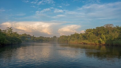 Obraz premium Calm river reflecting the sky with clouds and trees lining the banks in a scenic landscape view