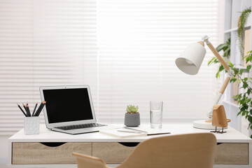 Stylish workplace with laptop and stationery on white table in office