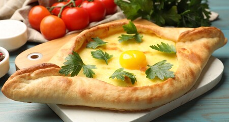 Tasty khachapuri with cheese, egg, parsley, tomatoes and spices on light blue wooden table, closeup
