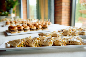 Appetizer wraps and mini burgers on trays at event