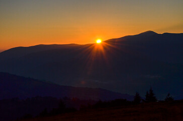 Morning sun casts warm hues across majestic range of dark blue mountains casting a warm glow on the...