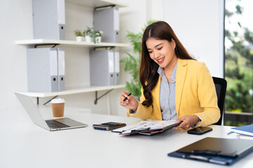 Computer and papers. Focused asian woman office worker do paperwork manage documents. Young lady accountant reviews expenses.