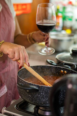 Woman cooking ravioli in red meat sauce with glass of wine
