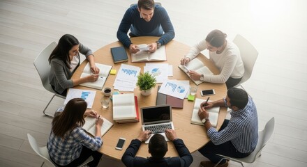 Overhead view of a business meeting with people around a table with laptops and documents spread out