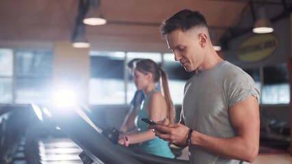 Smile young man use phone on a treadmill in gym sportsman sport fitness internet face technology fit lifestyle male workout athlete sportswear networking body exercise healthy mobile smartphone - Powered by Adobe