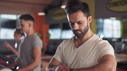 Portrait man on a treadmill in gym look on smartwatch sportsman sport fitness internet face technology fit male smile workout athlete sportswear networking body exercise healthy young slow motion - Powered by Adobe